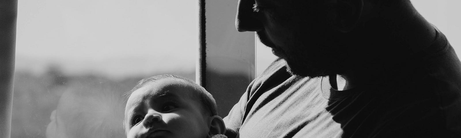 black and white photo of male holding infant baby in arms with strong shadowing