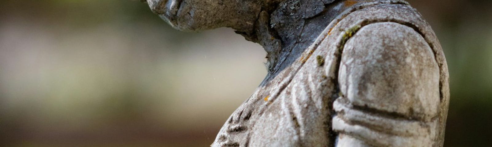 A graveyard statue, lady in a dress, with her head bowed, the statue neck looks damaged as the head peer downward.