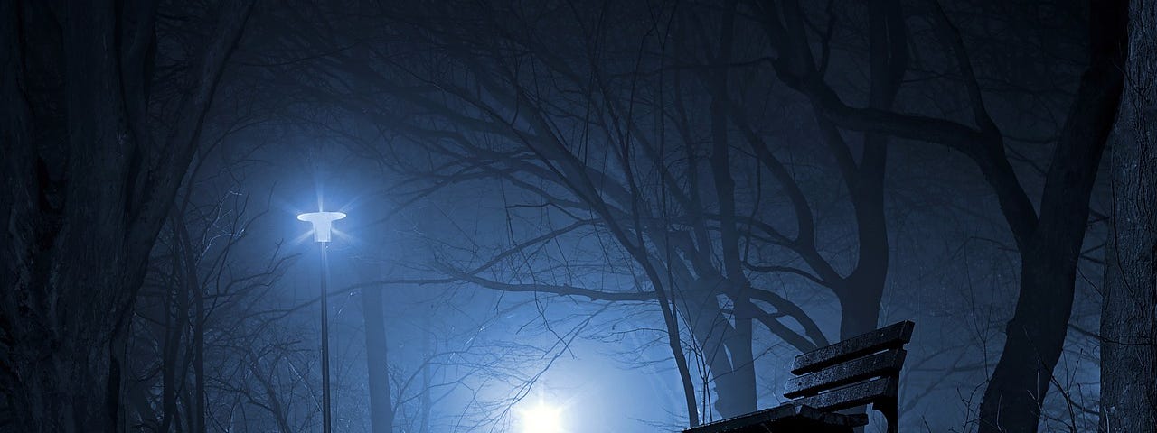 A foggy night, lonely and still, with an empty park bench and a solo streetlight.
