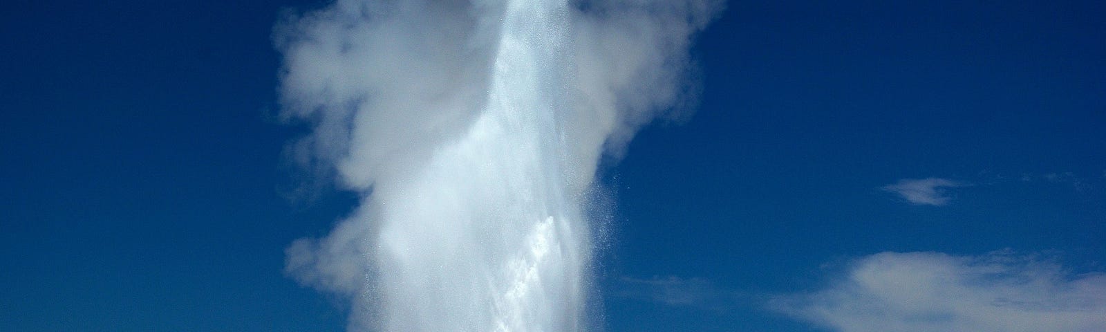 Old Faithful, a geyser in Yellowstone National Park in the US, shoots water into a blue sky.