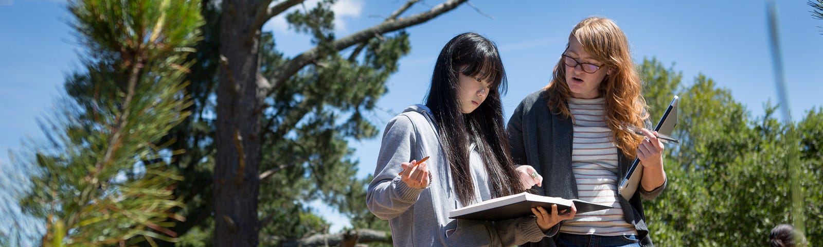 A female teacher works with a female student during an outdoors learning activity.