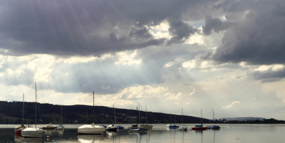 Sunlight slanting down from cloudy sky over lake with moored sailboats