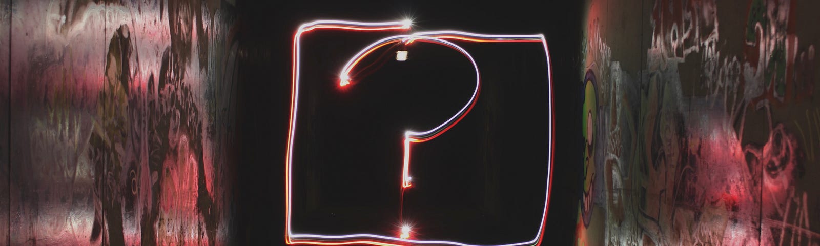 A picture of a neon lit question mark at the end a dark corridor. Photo credit: Emily Morter on Unsplash