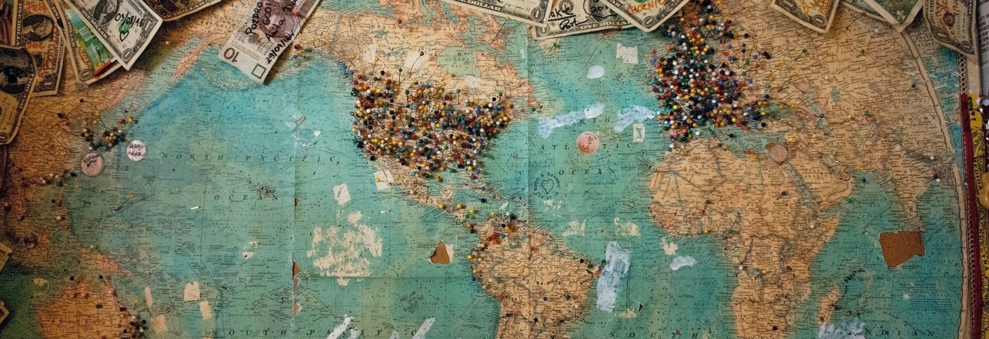 A old-looking map with lots of pins in Europe and North America and a bunch of money in different currencies lying around it