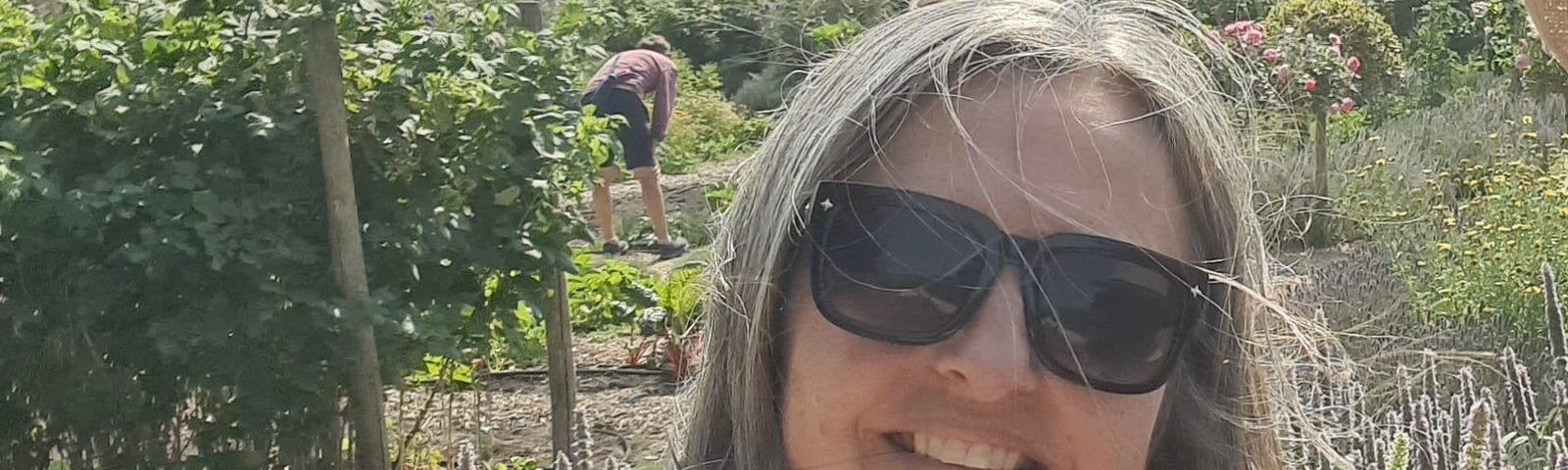Lisa in a sunny garden, with someone digging in the background.