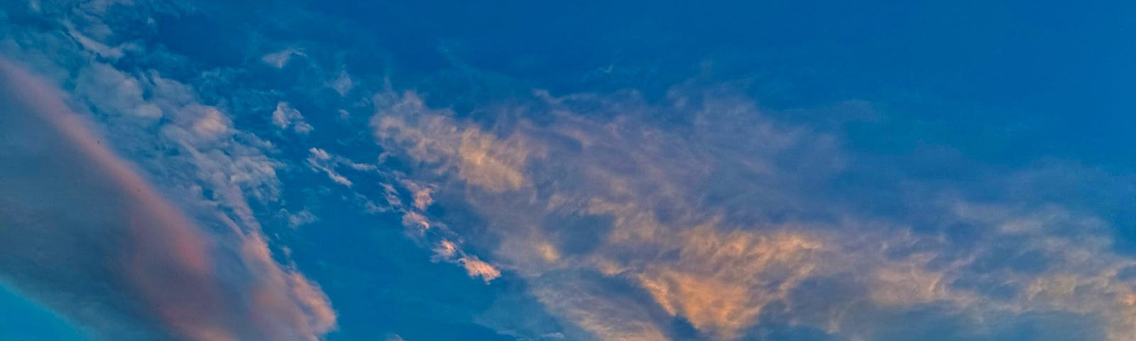 Wind swept clouds at sunrise show gold through lavender against a blue sky which becomes turquoise near the horizon.