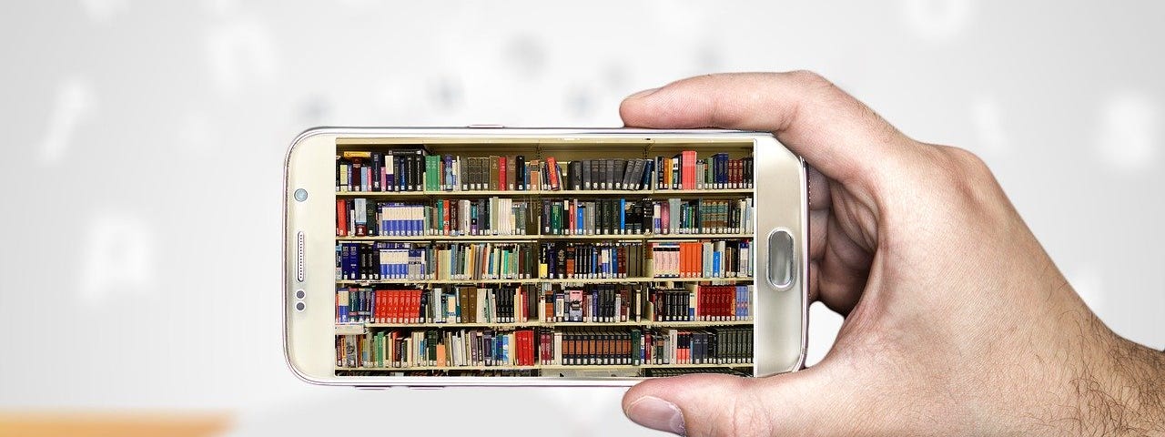 Hand holding a cell phone with shelves of books in the screen.