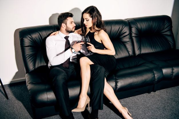 A boss and his employee sit on an office couch embracing.