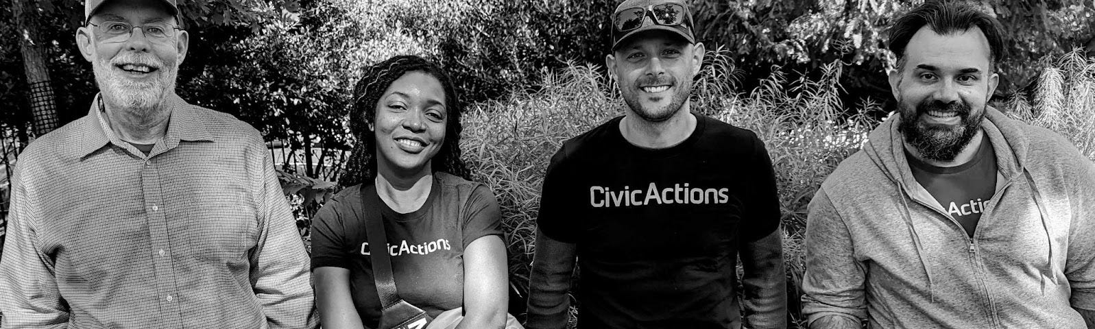 Four people stand side by side in front of trees, two of whom wear CivicActions t-shirts