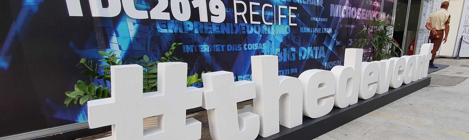 Imagem mostra painel escrito TDC2019 RECIFE e #thedevconf no chão com letras de madeira