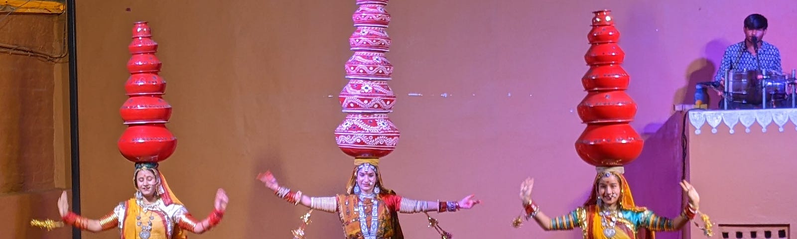 Photo of 3 women dancing in traditional Rajasthani attire with several pots balanced on their heads