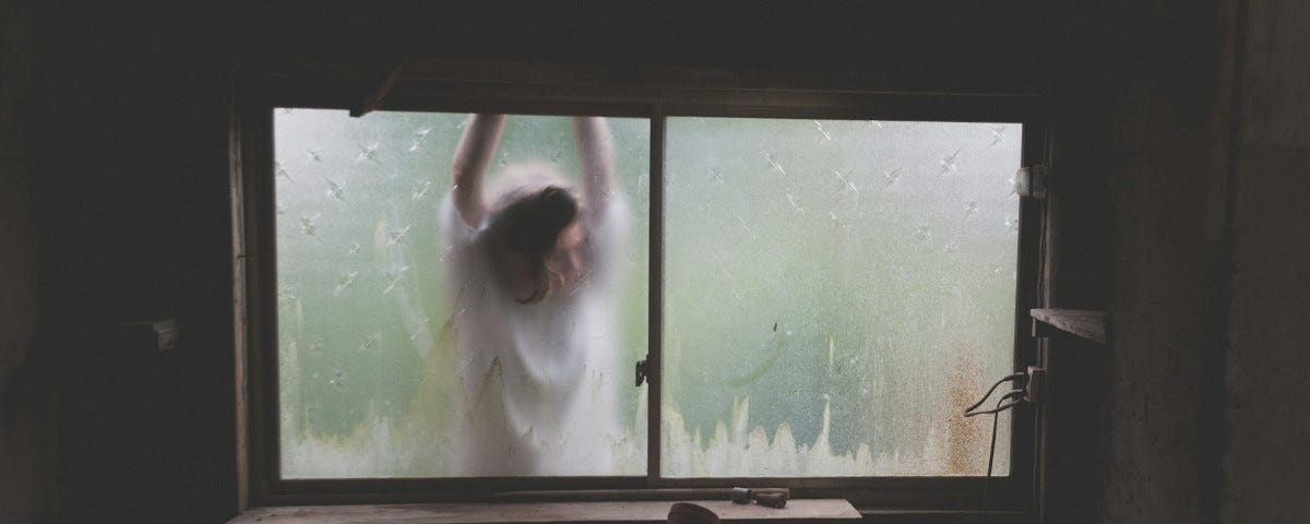 Looking out through the filthy window of a garden shed, a woman can be seen, her face pressed against the glass. She is wearing a white dress and veil. Her arms are raised in a way which suggests her wrists — unseen — may be tied to each other and to the shed.