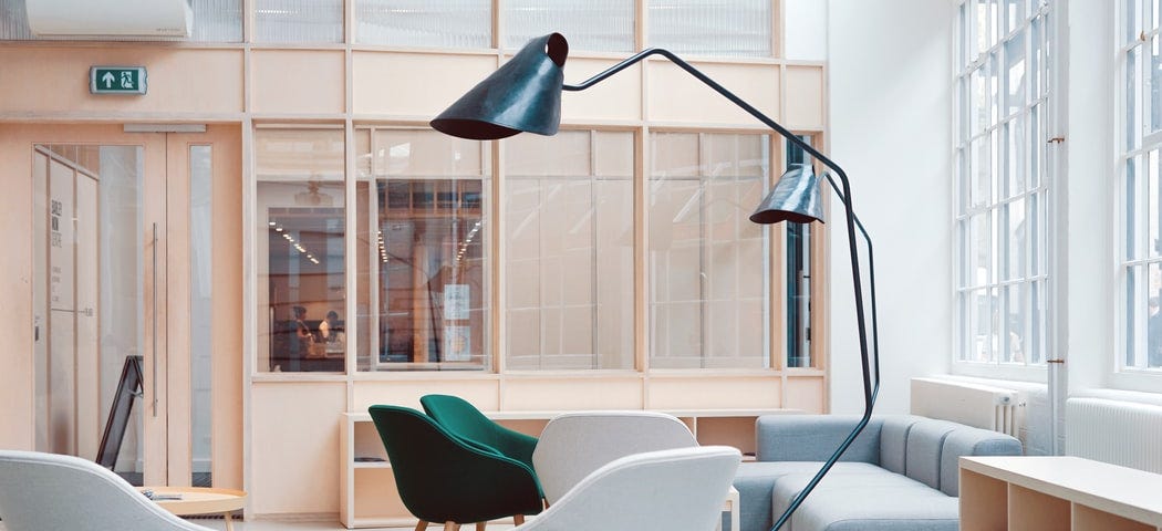 An office lounge area with blue rugs, grey and green chairs and a modern grey couch