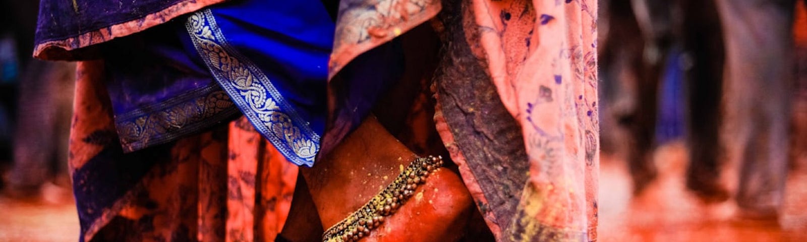 A cropped image of a woman’s feet standing in a shallow puddle with wide silver anklets and an overhanging sari.