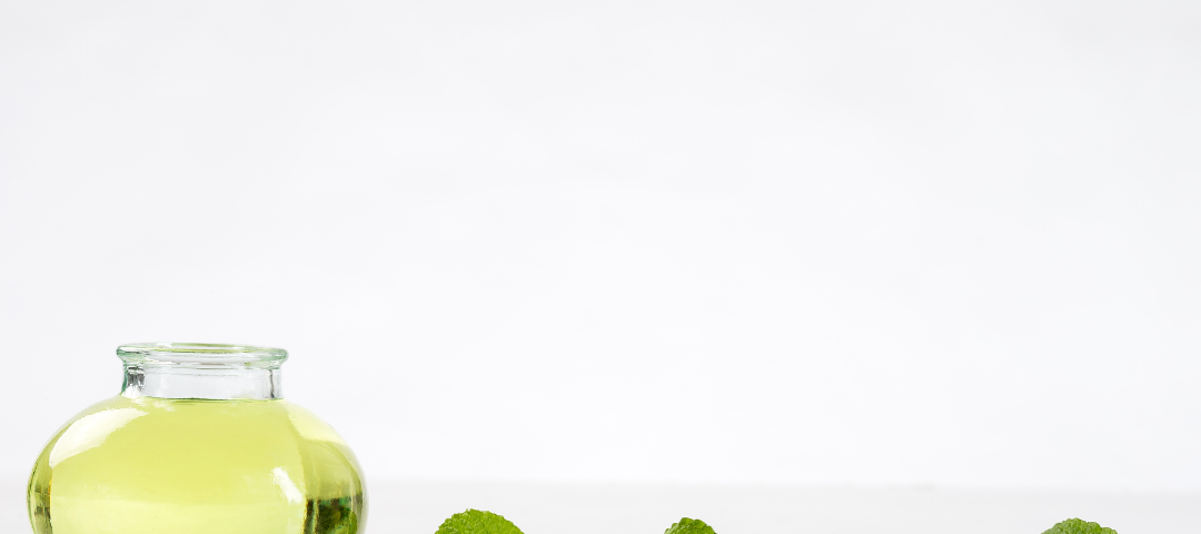 Container of peppermint oil with peppermint leaves trailing behind it.