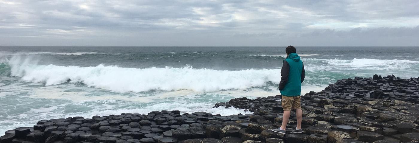 A photo of Aaron on a pebbled beach looking out over the sea.