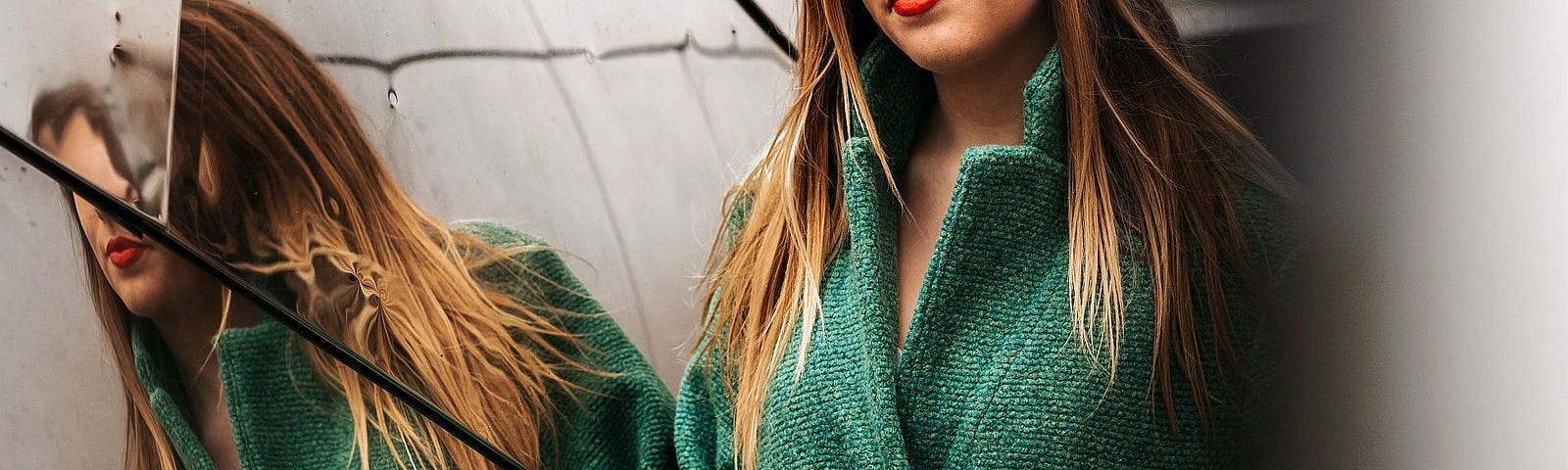 Woman in a green coat standing next to a mirror