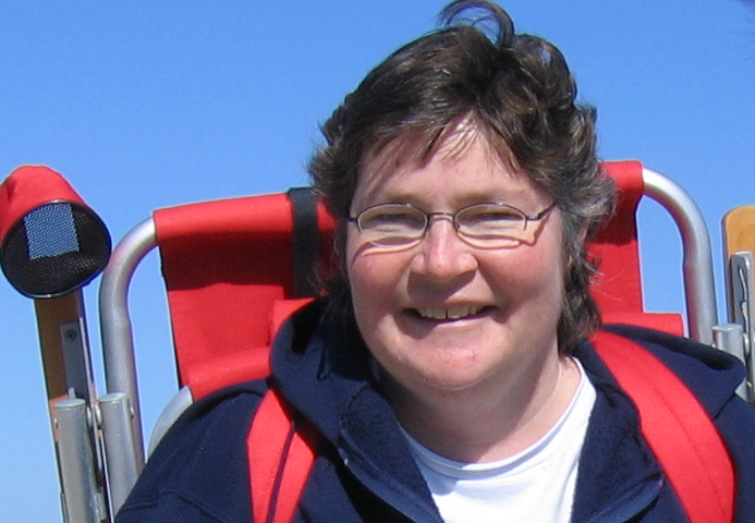 Denise Kendig smiling at camera with red beach chair backpack and blue skies
