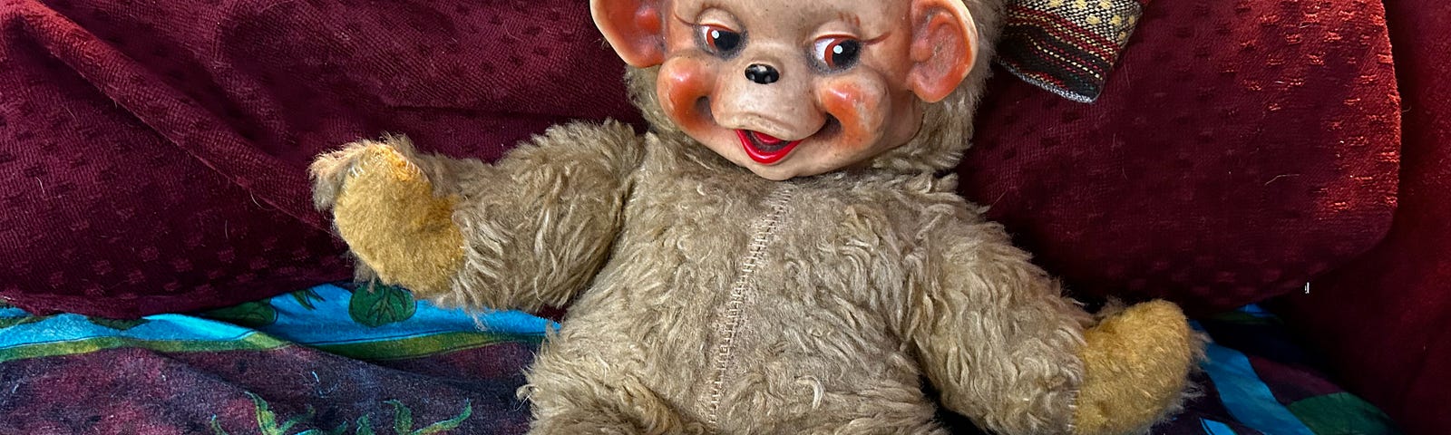 A toy monkey with a plastic face lounges on a burgundy pillow