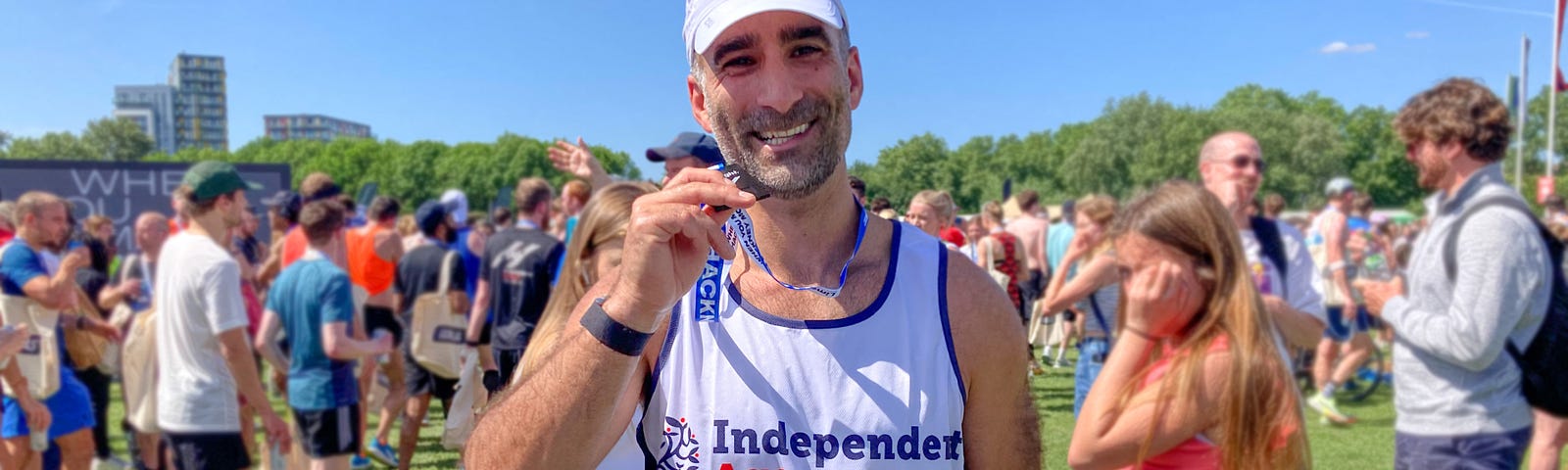 A man smiles at the camera as he holds up a medal. He’s wearing an Independent Age running vest and cap.