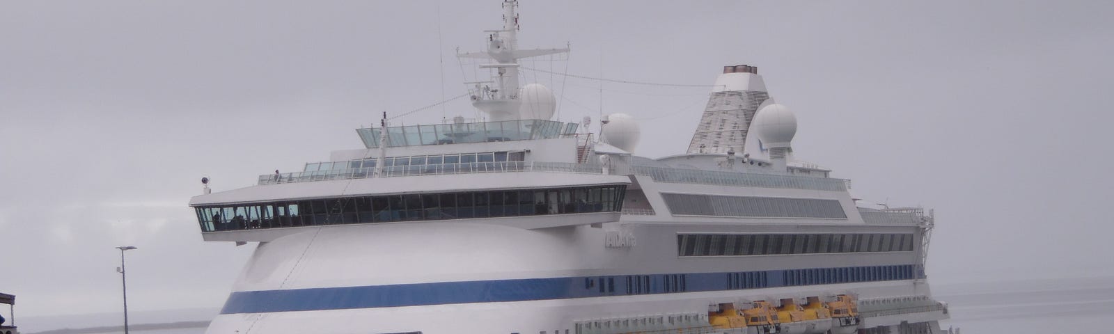 A mid-sized luxury cruise ship with rakish lines and a modern abstract paint job (squiggly zigzags, big eyes, and big pouty red lips painted on the bow) berths in Iceland.
