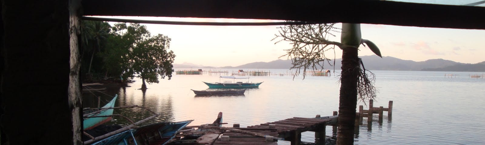 Looking through a window at a ramshackle dock and the sea with small outrigger fishing boats and big bamboo fishing structures scattered around