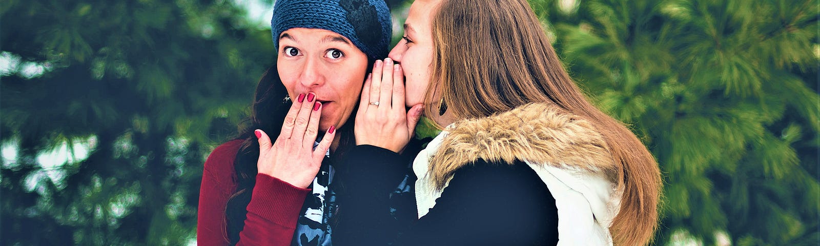 girl whispering into another girl’s ear