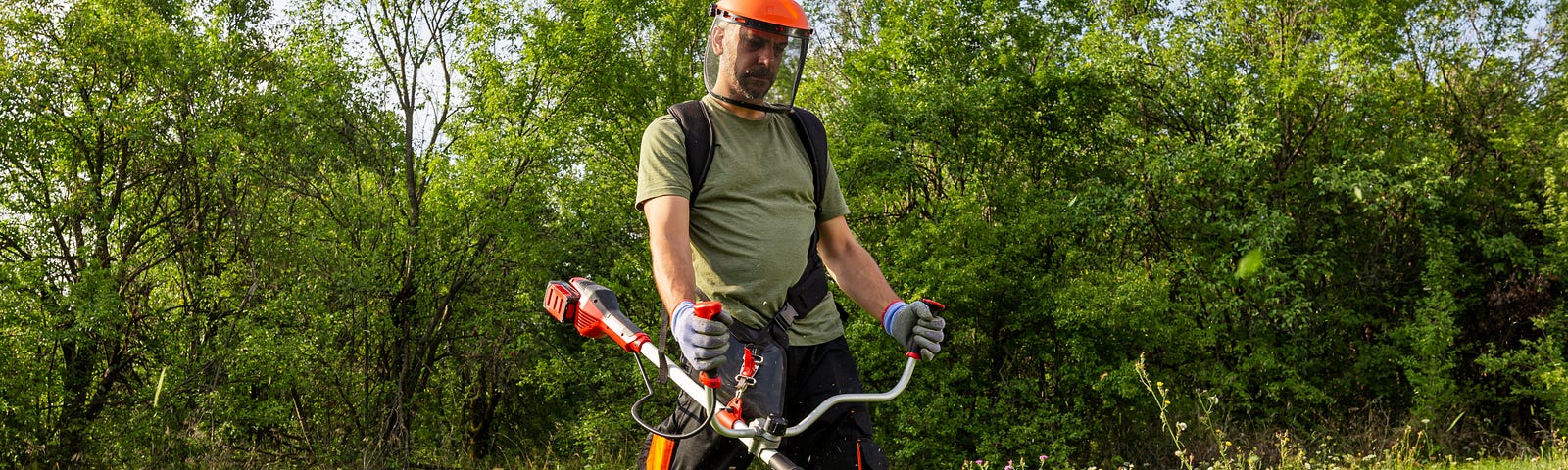 Man cutting grass in protective helmet and gloves