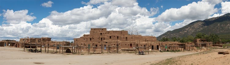 Taos Pueblo occupies the whole image space with fluffly white clouds and blue sky in the background.
