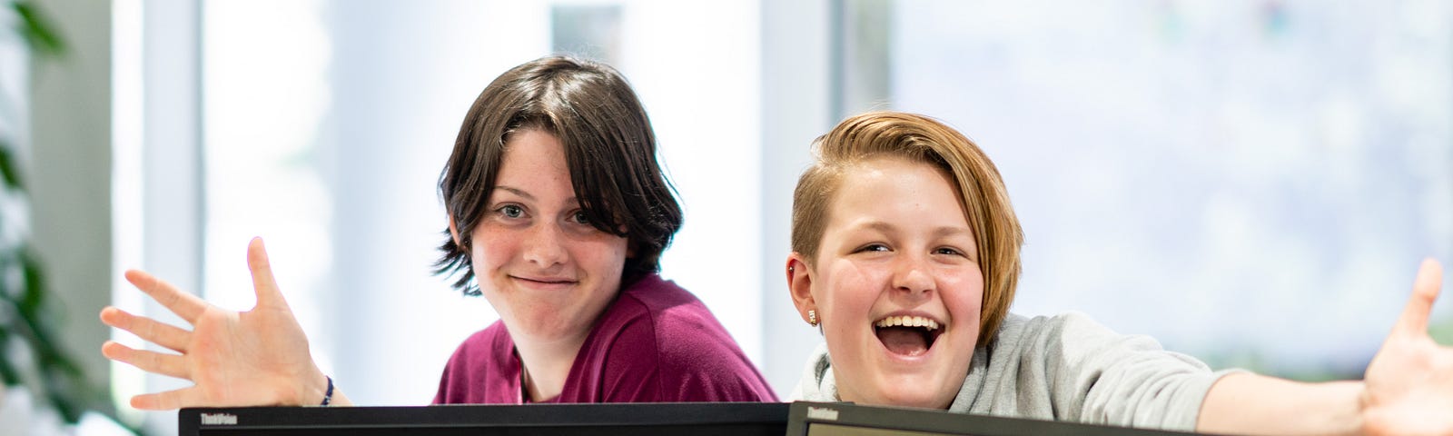 Two young people with their hands out smiling behind two laptop monitors