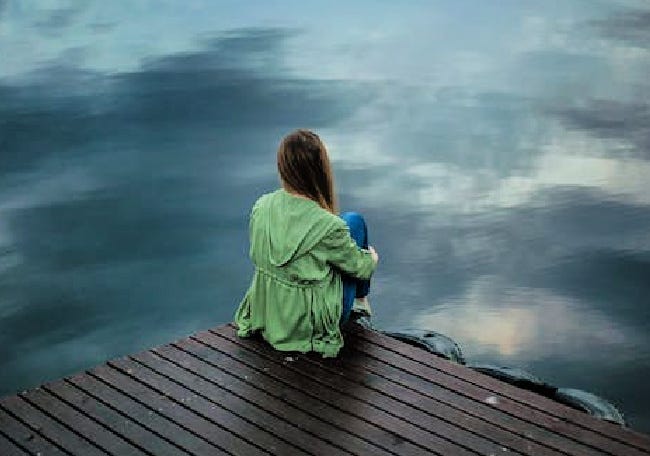 A woman wearing a green jacket sitting on a pier.