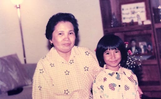 A Filpina elder with her arm around a Filipinx child. Both are wearing pink button up shirts with patterns and shapes.