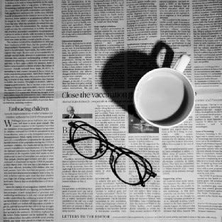 Optical glasses and coffee mug sitting on a newspaper.