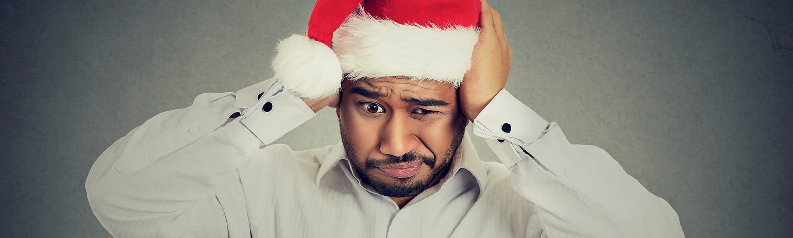 Man in Santa hat holding his ears with a frustrated look on his face. (holidays, relationships, family, uncomfortable conversations, awkward questions, conflict)