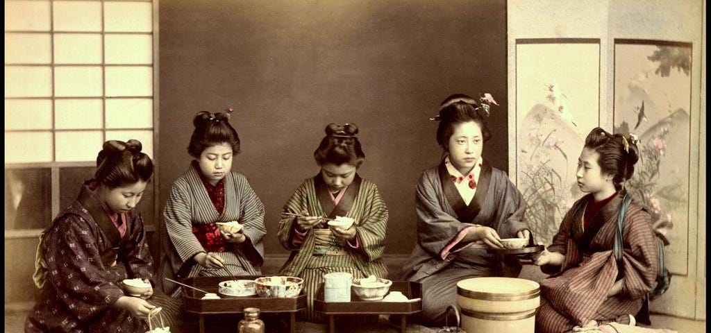 Five pre-modern Japanese women in kimono and old-fashion hairstyles eating lunch together.