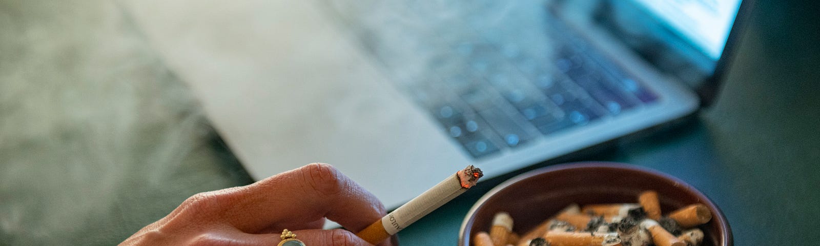 A person holding a cigarette in  in front of her laptop.