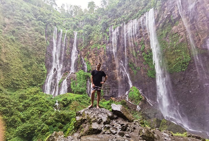man standing on top of mossy rocks in front of multiple waterfalls