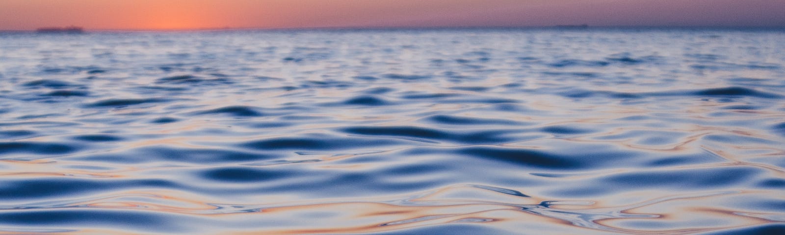Pinkish, blue horizon above a deep, dark ocean.