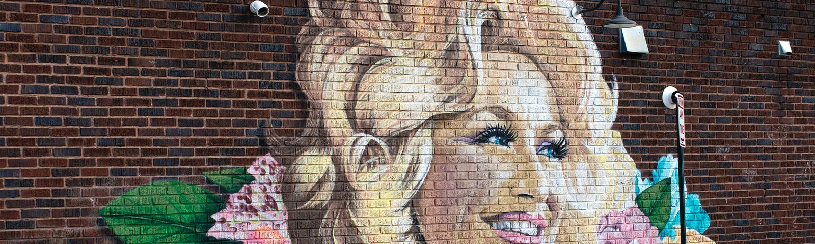 A mural of Dolly Parton is painted on a brick wall. She has bright flowers painted behind her.