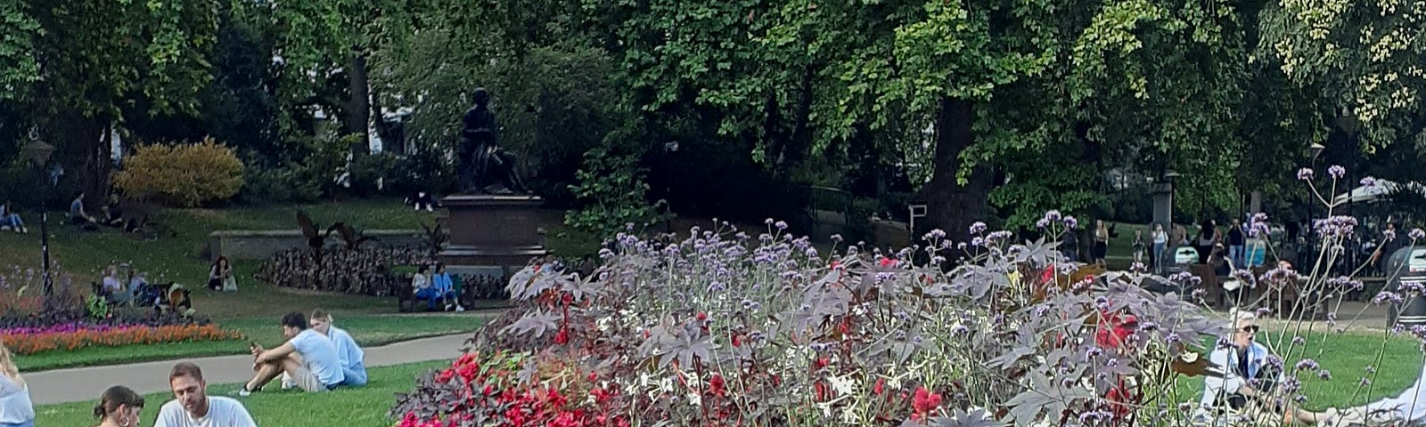 A flower bed in a city park with people sitting nearby.