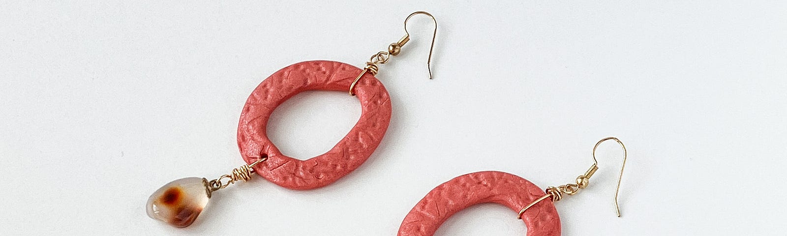 Pink polymer clay hoop earrings with carmine stones on a white background