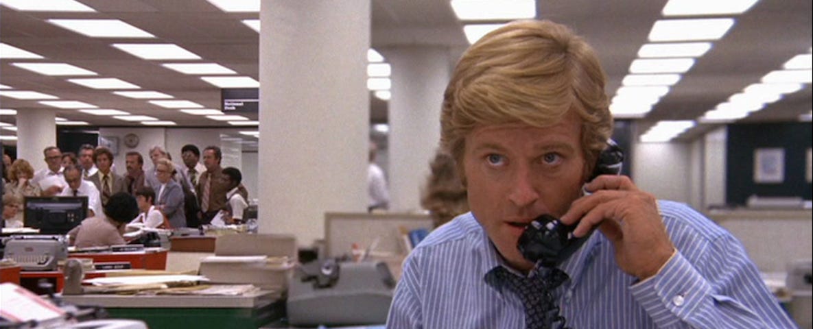 Still from the movie All the President’s Men. Robert Redford is on the telephone in a newsroom.