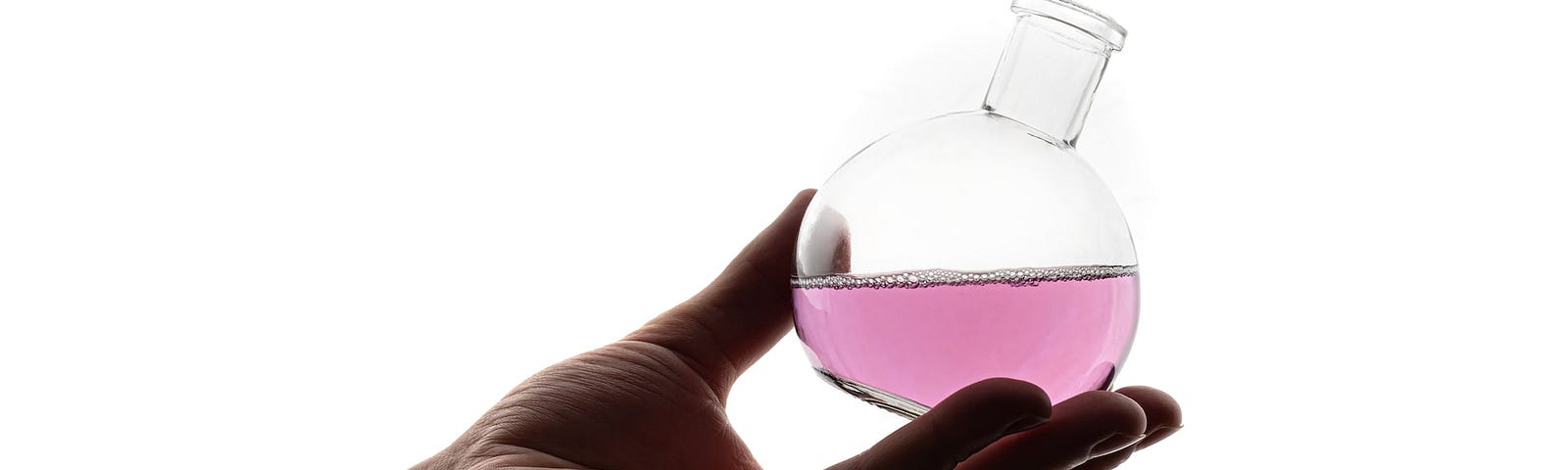 IMAGE: On a white background, a hand holding a lab flask with a pink liquid