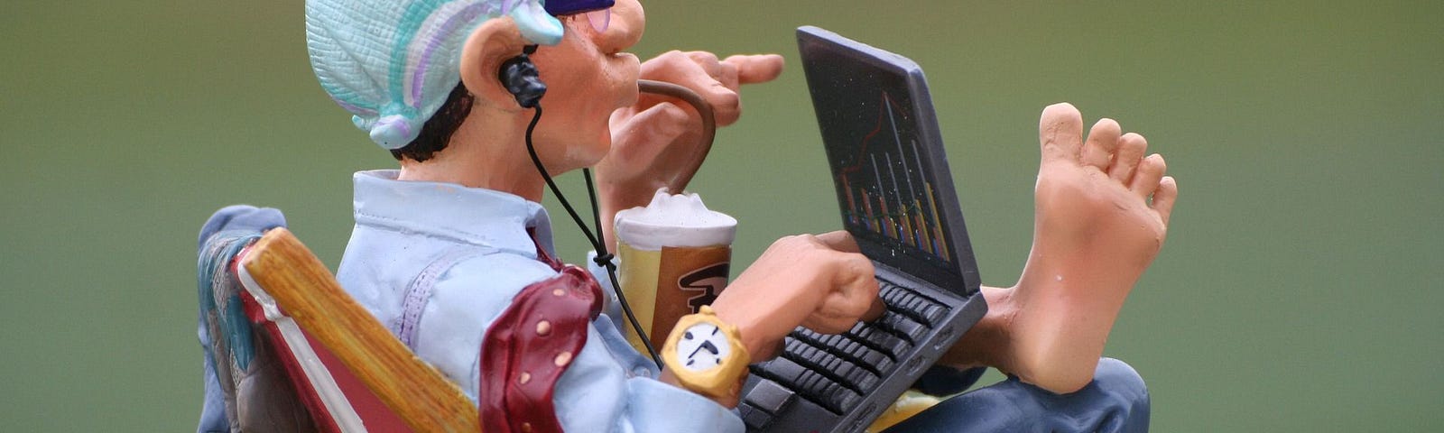 Claymation figure of a man sitting in a lounge chair barefoot while working on a laptop computer.