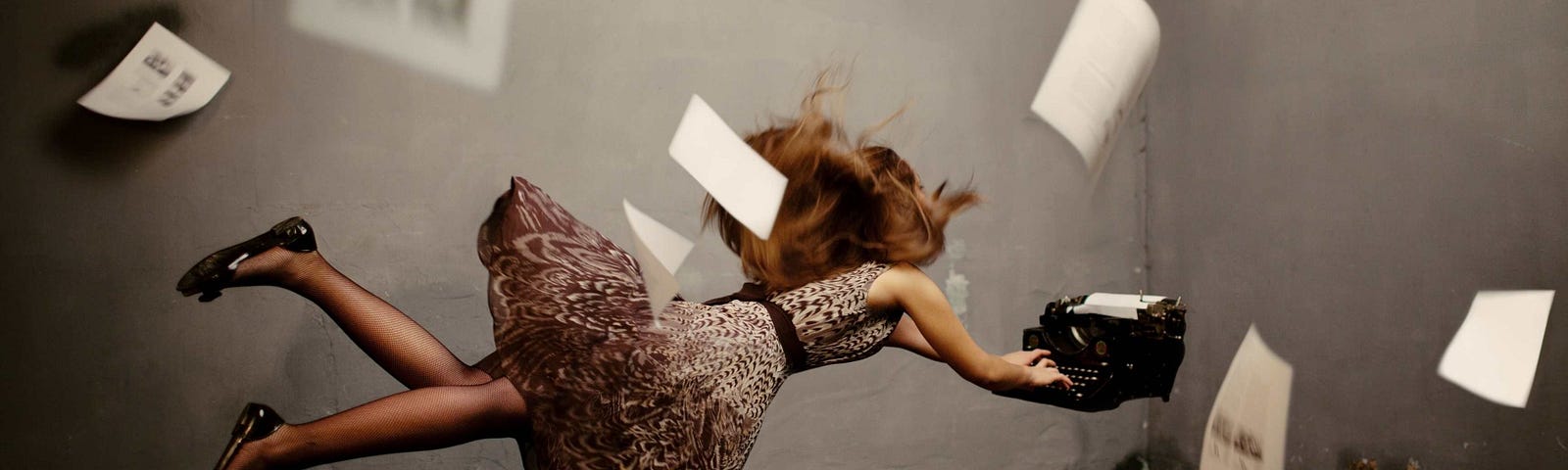 woman floating in air wearing a dress typing on a typewriter while blurry papers fall around her