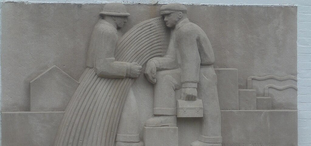 A carved stone frieze of two working people facing each other with a caption carved below: “isnsure domestic tranquility.”