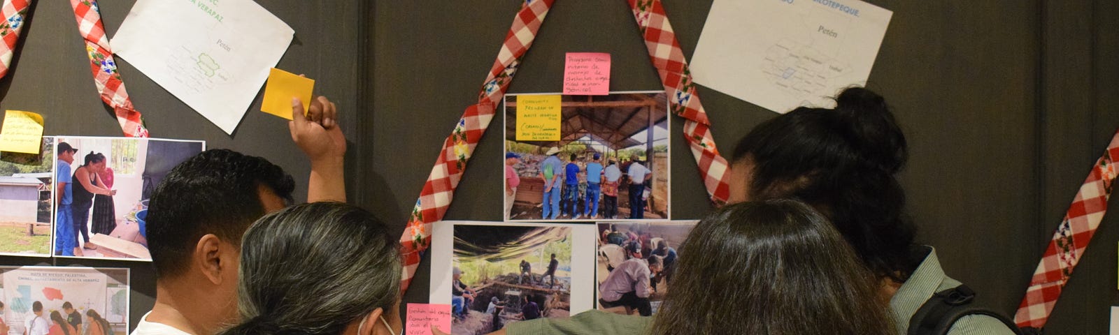 A group of four people at a workshop, discussing photos and post-it notes which are stuck on a wall.