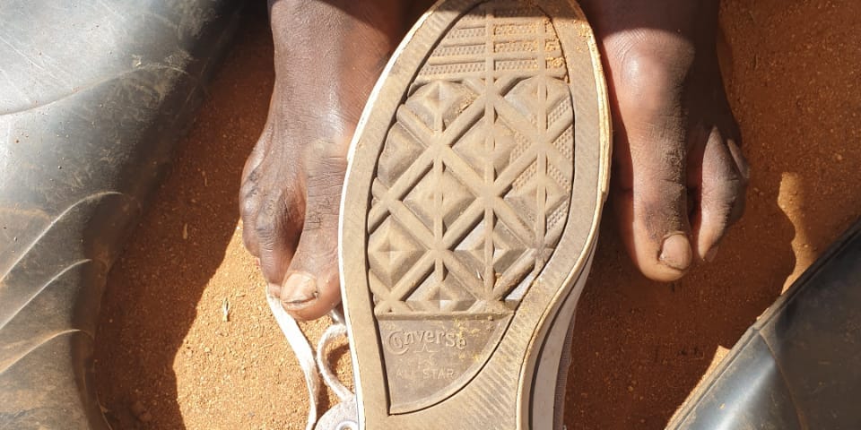 African male feet, a converse shoe and gumboots with soil in the background.