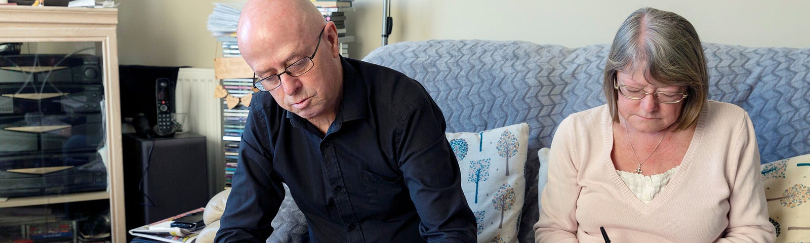 Photo of a man and woman sat on a blue sofa whilst filling out paperwork.