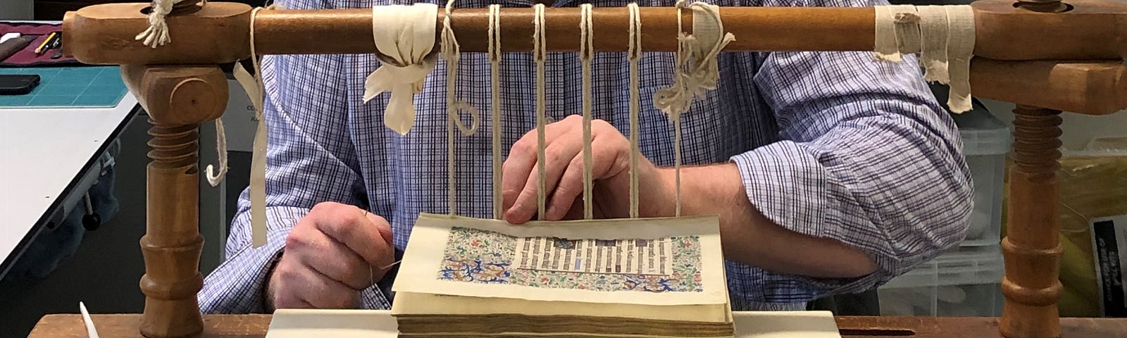 A conservator re-sewing an illuminated Latin manuscript on a traditional sewing frame